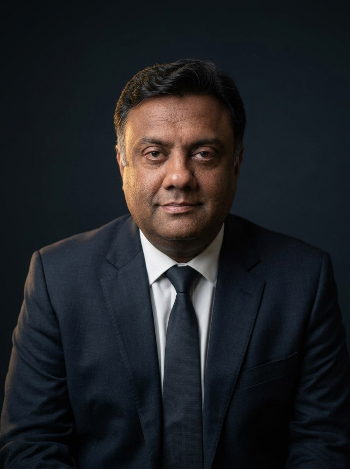 Portrait of Syed Aun Mohammed Bokhari, Barrister-at-Law, in a dark suit against a deep charcoal background